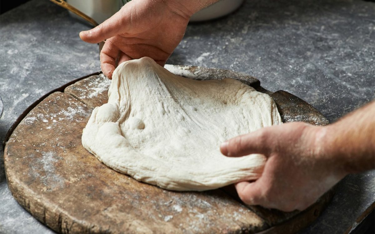 someone shaping dough for pizza
